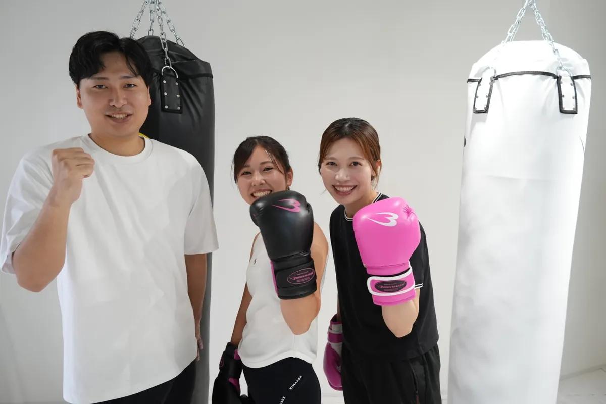 サンドバッグの前で笑顔を見せるトレーナーと会員